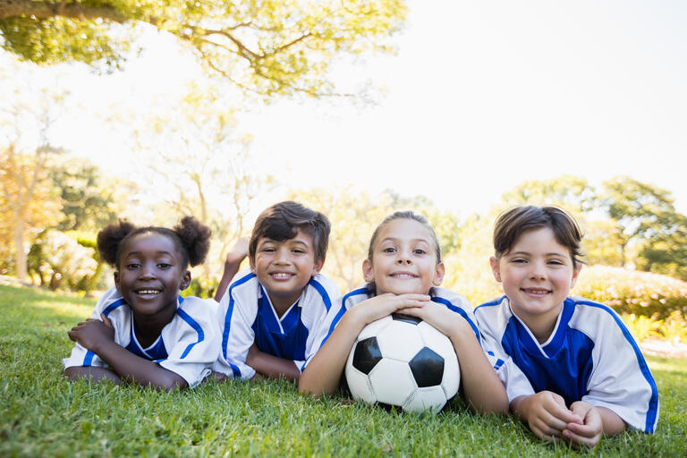 children soccer team smiling at camera while lying on the floor in park